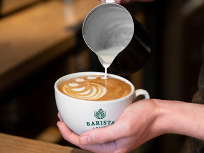 Barista schenkt latte art in een kop van Barista Cafe
